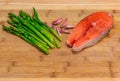 Fresh salmon steak surrounded with garlic and asparagus on a wooden cutting board Royalty Free Stock Photo