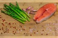 Fresh salmon steak surrounded by pink peppercorns, Himalayan salt, garlic and asparagus on a wooden cutting board Royalty Free Stock Photo