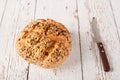 Fresh seedy bread with knife on a white wooden