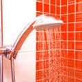 Fresh shower where Water running from shower head and faucet in modern bathroom with orange wall Royalty Free Stock Photo