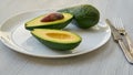 Fresh sliced avocados on the white plate. Healthy vegetarian diet food on gray background with copy space