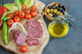 Fresh sliced fuet, tomatoes cherry and some vegetables on the kitchen cutting board. Olives in wooden bowl, olive oil in glass Royalty Free Stock Photo