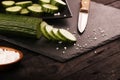 Sliced green cucumbers with knife and salt on black plate and black wood rustic table