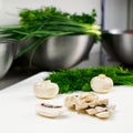 Fresh sliced mushrooms on a cutting board. In the background are green onions, parsley and dill in a stainless steel bowl Royalty Free Stock Photo