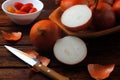 Fresh and sliced organic onions on wooden bowl and scattered over rustic wooden table in kitchen Royalty Free Stock Photo