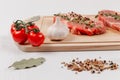 Sliced raw pork steaks with seasonings, tomatoes, bay leaf and thyme on a cutting kitchen board on a white wooden table Royalty Free Stock Photo