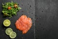 Fresh sliced salmon fillet with arugula and lemon on slate plate, top view