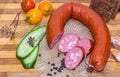 A fresh sliced smoked sausage horseshoe shape with bacon and sliced green cucumber and three red and yellow tomatoes Royalty Free Stock Photo