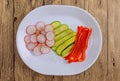 Fresh sliced vegetables lie on a plate on a wooden background. Vegetables seasoned with spices: salt, black and red ground pepper, Royalty Free Stock Photo