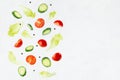 Fresh sliced vegetables for summer salad - cucumber, cherry tomato, green salad - flying on soft light white wall, border. Royalty Free Stock Photo