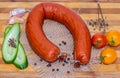 A fresh smoked sausage horseshoe shape with bacon and sliced green cucumber and three red and yellow tomatoes cherry and Royalty Free Stock Photo