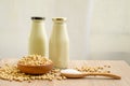 Fresh soybean seeds in brown wooden bowl with sugar in spoon and two bottles of soy milk on the table