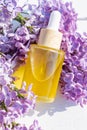 Fresh sprig lilac flowers and bottle with cosmetic oil on a white background with copy space. Wellness, home skin care and spa