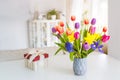 Fresh spring colorful bouquet of tulips, daffodils, irises in vase and gift box on white table with light classic design Royalty Free Stock Photo