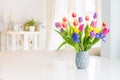 Fresh spring colorful bouquet of tulips, daffodils, irises in vase standing on white marble table with light classic design living Royalty Free Stock Photo