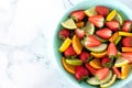 Fresh spring fruit salad with strawberries, orange, lemon, lime, green apple, and spinach leaves on white marble table, top view Royalty Free Stock Photo