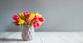 Fresh spring yellow and pink tulips bouquet in blue vase standing on black wooden table with gray background. Festive flowers for Royalty Free Stock Photo