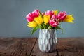 Fresh spring yellow and pink tulips bouquet in blue vase standing on rustic wooden table with gray background Royalty Free Stock Photo