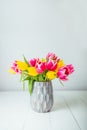 Fresh spring yellow and pink tulips bouquet in blue vase on white wooden table with white background. Festive flowers Royalty Free Stock Photo