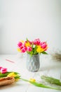 Fresh spring yellow and pink tulips bouquet in a vase, other flowers and details on florist workspace on white wooden table.