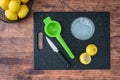 Fresh squeezed lemon juice in a drinking glass, lemon halves, paring knife, citrus press, on a black cutting board