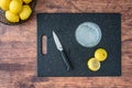 Fresh squeezed lemon juice in a drinking glass, lemon halves, paring knife, on a black cutting board, wood table