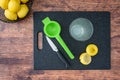 Fresh squeezed lemon juice in a drinking glass, lemon halves, paring knife, citrus press, on a black cutting board