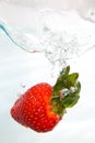 Fresh strawberri splashing into water on white