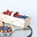 Fresh strawberries and blueberries lie in a plate and basket on a glass table against the background of a plastered white wall. Fo Royalty Free Stock Photo