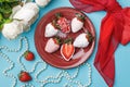 Fresh strawberries coated with white and pink chocolate lie on a red plate on a turquoise background Royalty Free Stock Photo