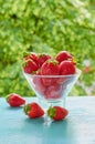 Fresh strawberries in a glass bowl on the blue kitchen table on the blurred nature background. Tasty vegan summer dessert Royalty Free Stock Photo