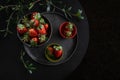 Fresh strawberries lie in a black handmade cup and plate on a black round table surrounded by green twigs, dark photo Royalty Free Stock Photo