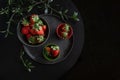 Fresh strawberries lie in a black handmade cup and plate on a black round table surrounded by green twigs, dark photo Royalty Free Stock Photo