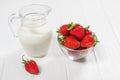 Fresh strawberries and milk jug on white wooden table