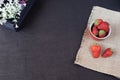 Fresh strawberries in mini metal bucket on hessian jute. White and purple flowers in a decorative wooden crate. Black background.