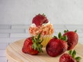 Fresh strawberries on a round wooden cutting board with a strawberry shortcake cupcake on a white subway tile counter with a Royalty Free Stock Photo