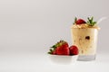 Fresh strawberries in a white saucer and tiramisu in a glass glass on a white background