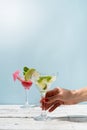 female hand with nice red manicure holding fresh summer cocktail with strawberry, lime and ice cubes on blue background Royalty Free Stock Photo