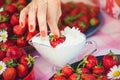 A fresh strawberry with cream in a bowl on a table in a summer garden is decorated with chamomile flowers the hand takes with a lo Royalty Free Stock Photo