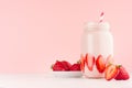 Fresh strawberry milk dessert for breakfast in jar with ripe berry on saucer, straw on pastel pink wall and white wooden table. Royalty Free Stock Photo