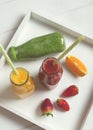 Fresh strawberry, orange and broccoli smoothie in bottles with straws fruits and vegetables on a white wooden rustic background, v Royalty Free Stock Photo