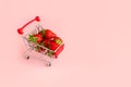 Fresh strawberry in shopping cart on pink background. Online shopping and Valentines Day minimalistic concept.