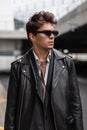 Fresh stylish portrait of a young man hipster in stylish sunglasses with a fashionable hairstyle in trendy black clothes in the Royalty Free Stock Photo