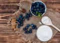 Fresh summer blueberry with leaf in the white bowl, flour in the bowl, wooden spoon on the brown wooden background