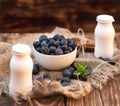 Fresh summer blueberry with leaf in white bowl, two yogurts bottles on the brown wooden background Royalty Free Stock Photo