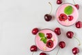 Fresh summer cherry yogurt with berries, oats and mint in glasses on white marble background. top view