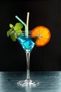 Fresh summer cocktail with blue curacao, ice, mint leaves, orange slice and two straws backlit on black background Royalty Free Stock Photo