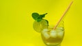 Fresh summer drink in glass, cocktail on yellow background, juice, alcoholic drink with ice and lime, straw Royalty Free Stock Photo