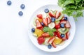 Fresh summer fruit and berry salad with strawberries, blueberries, banana, kiwi, orange, mint leaves and honey dressing, white Royalty Free Stock Photo