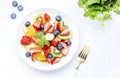 Fresh summer fruit and berry salad with strawberries, blueberries, banana, kiwi, orange, mint leaves and honey dressing, white Royalty Free Stock Photo